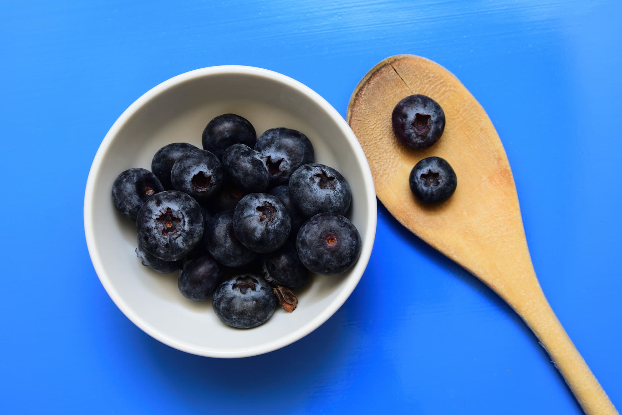 Fresh blueberries in a bowl and a wooden spoon.